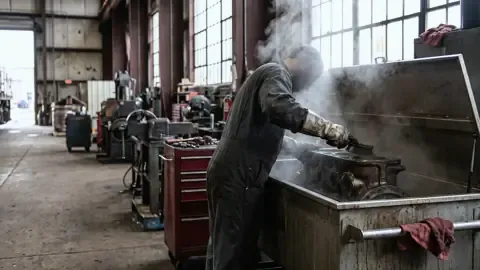 Degreasing a locomotive part in a solvent parts washer in a railroad shop