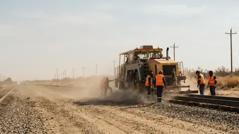 A railroad track crew replacing ties with a tamper in ballast dust
